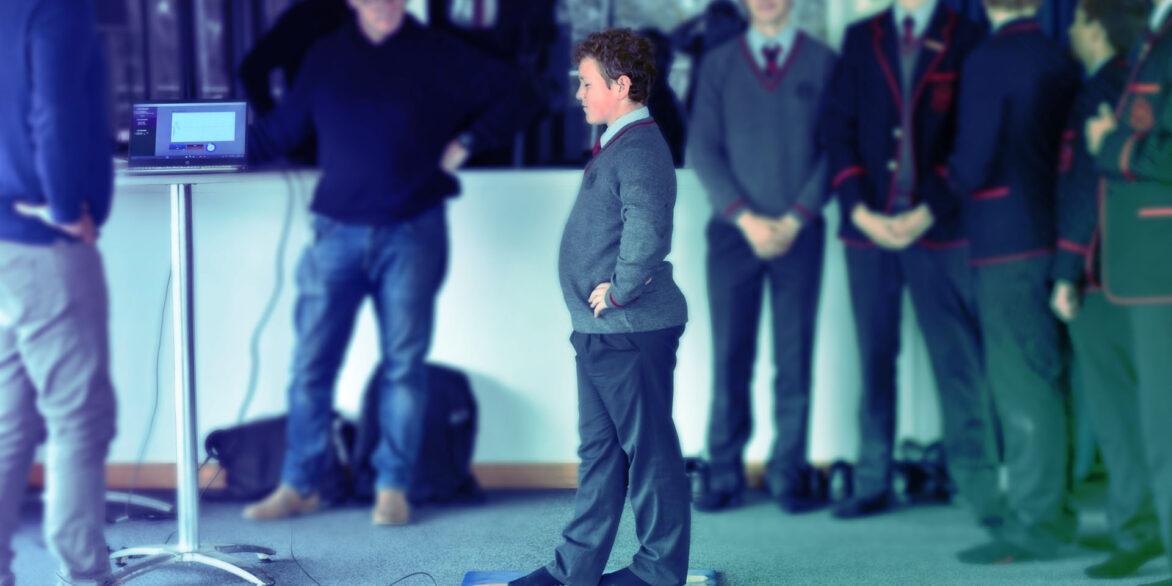 Child performing balance assessment on mat while supervised by instructor with monitoring equipment