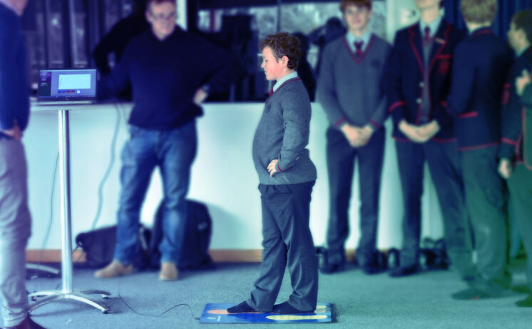 Child performing balance assessment on mat while supervised by instructor with monitoring equipment